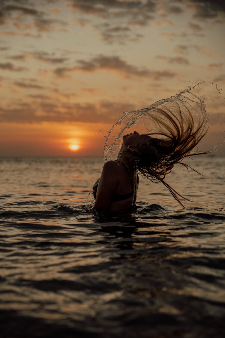 A Woman Flipping Her Hair In The Water During Sunset