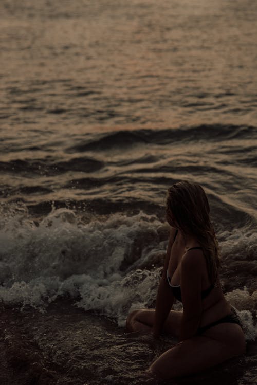 A Woman in Bikini Sitting at the Beach during Sunset