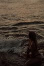 日落时分，一名女子穿着泳衣坐在海滩上，海浪在她周围轻轻拍打