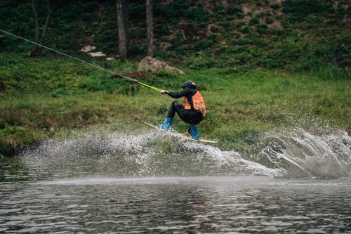Free A wakeboarder in action creating a splash as they perform tricks over water with lush greenery backdrop. Stock Photo