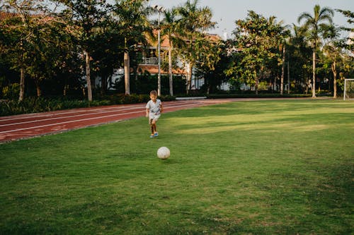 Мальчик в белой рубашке играет в футбол на поле зеленой травы