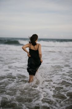 一名身穿黑色连衣裙的女子走过海浪，营造出宁静而略带忧郁的沿海氛围