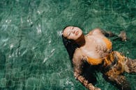 身穿黄色比基尼的亚洲女子在清澈的水中平静地游泳