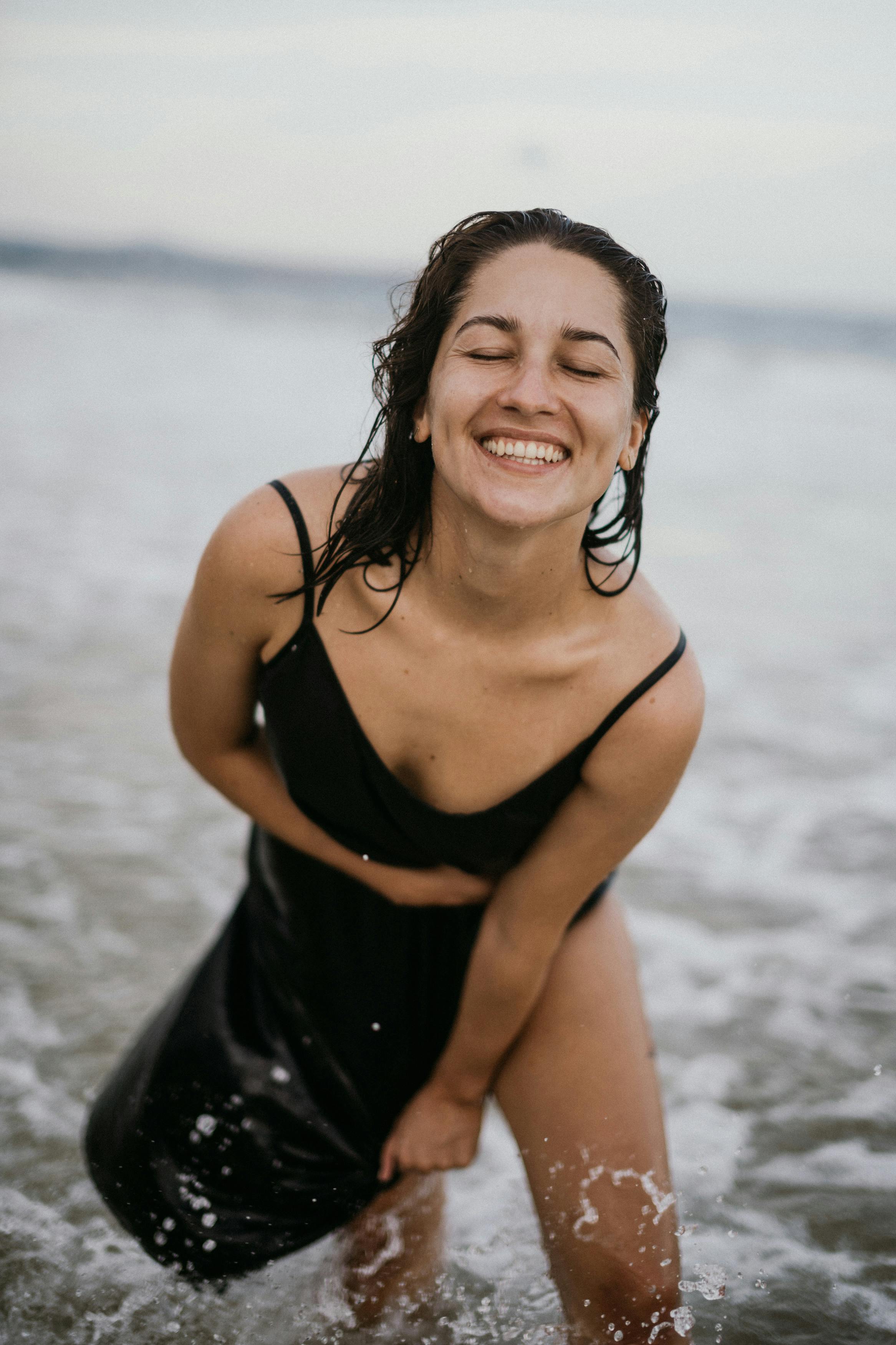 一名身穿黑色连衣裙的女子在海滩上欢声笑语，周围波涛汹涌