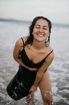 一名身穿黑色连衣裙的女子在海滩上欢声笑语，周围波涛汹涌