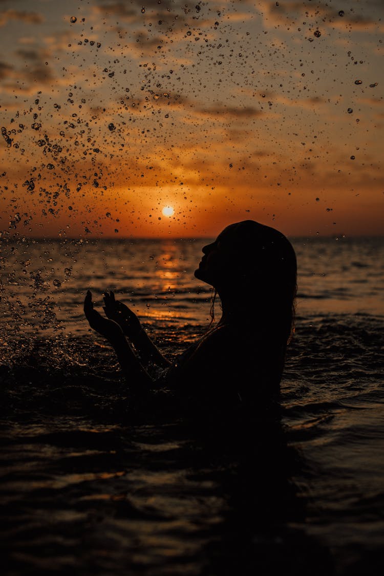 Silhouette Of A Woman Splashing Water In The Sea At Sunset