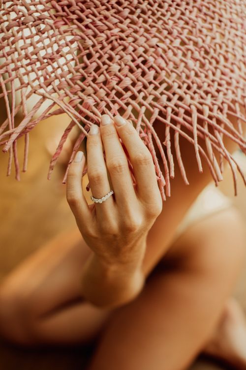 Free Close-up of a hand wearing a ring holding a woven straw hat, with a blurred background. Stock Photo
