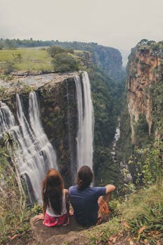 Couple sitting near a majestic waterfall enjoying nature's beauty together.