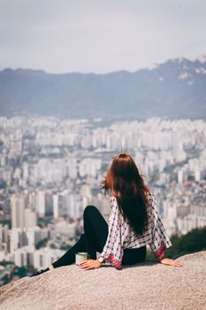 一名女子坐在岩石上，俯瞰韩国首尔的城市景观，冒险正等待着她