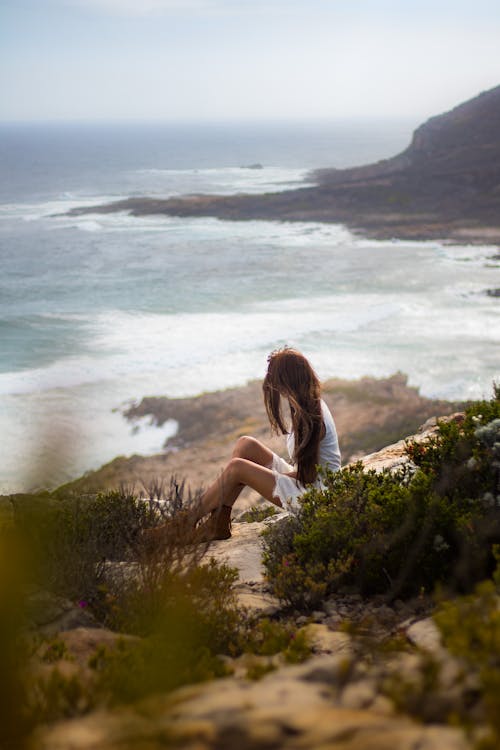 A Woman Sitting on a Cliff in a Coastal Landscape