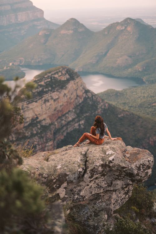Free Woman sits on a cliff edge in South Africa, gazing at a breathtaking mountain landscape. Stock Photo