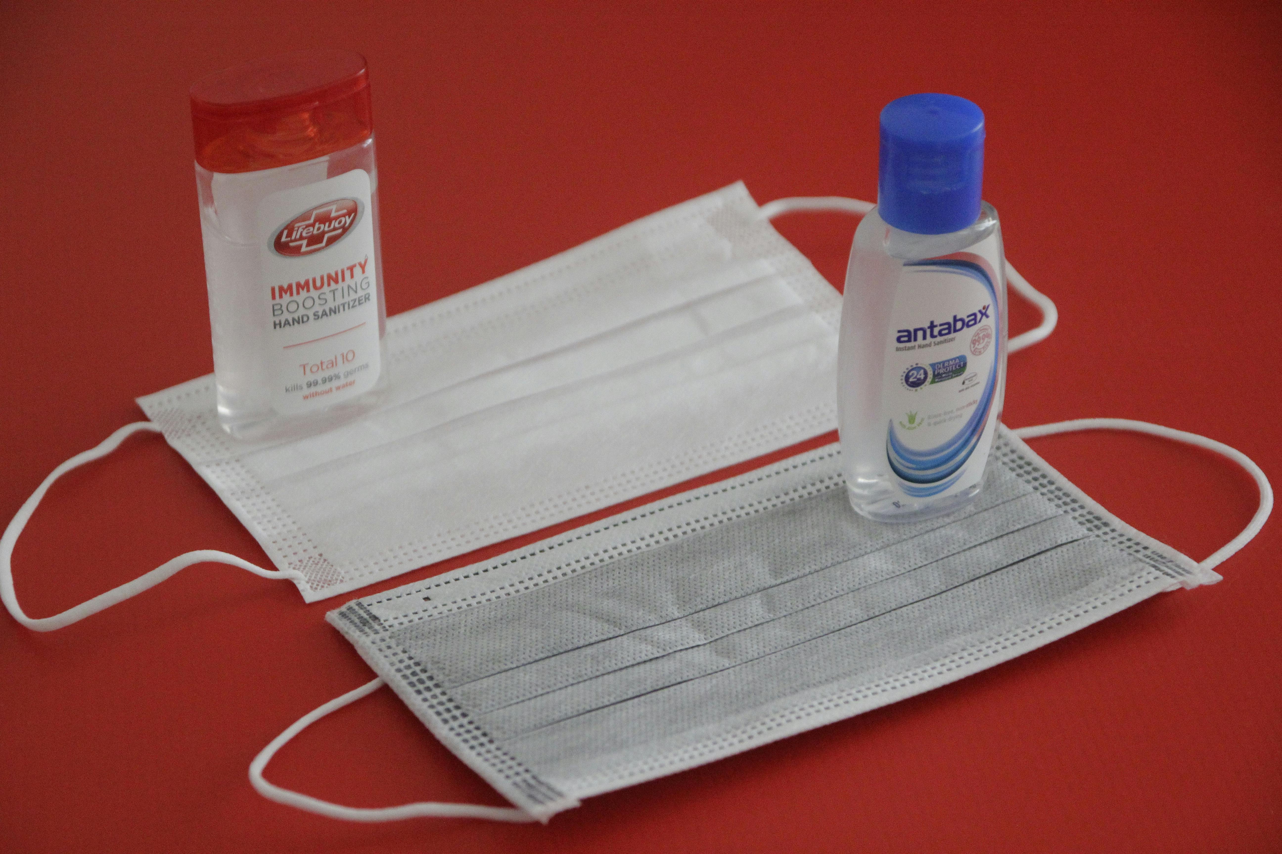 Close-up of face masks and sanitizers on a red surface, emphasizing hygiene.