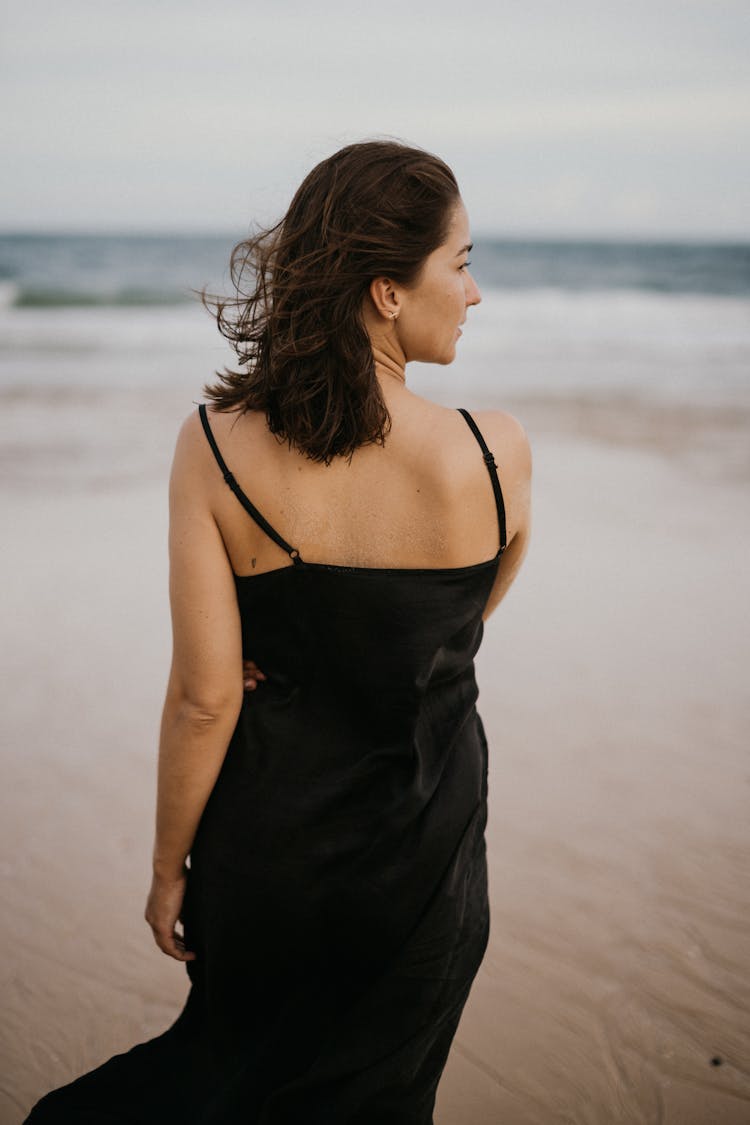  Back View Of A Woman In A Black Dress Walking On The Beach