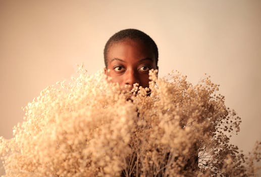 Minimalist portrait of a woman with short hair behind dried flowers, creating a serene and mysterious mood.