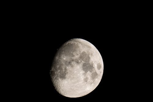 Black and white of grey craters on surface of big bright round glowing waxing Moon on black background