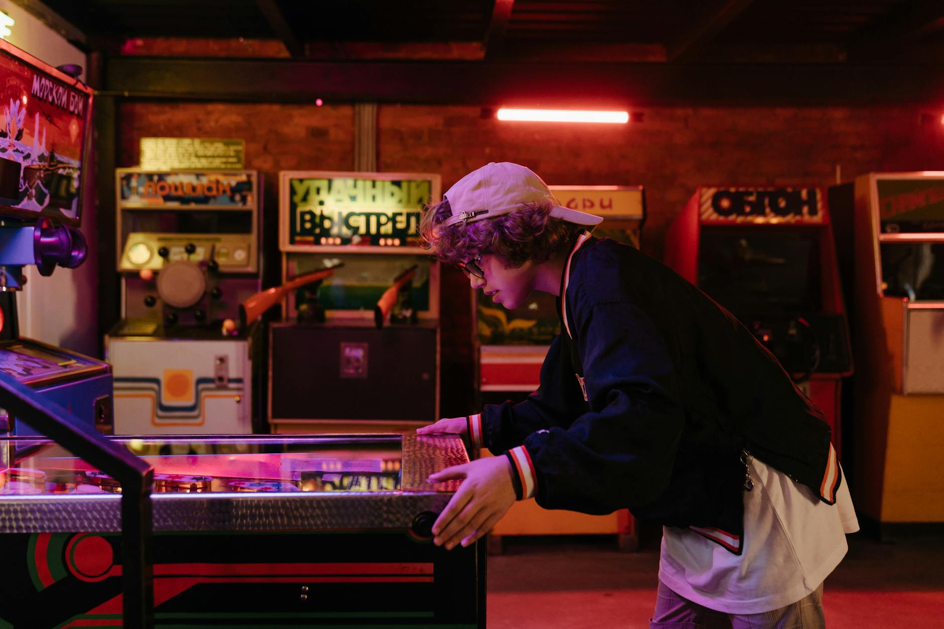 Teenager joyfully playing pinball in a nostalgic retro arcade setting.