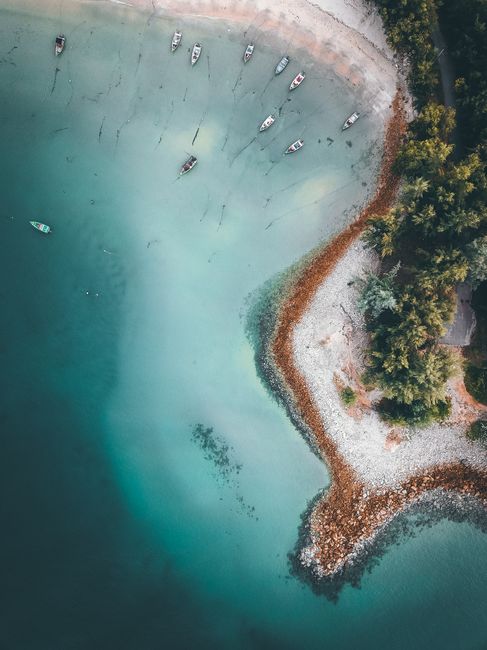 Breathtaking aerial view of boats floating in shallow water of sea near tropical shoreline with trees