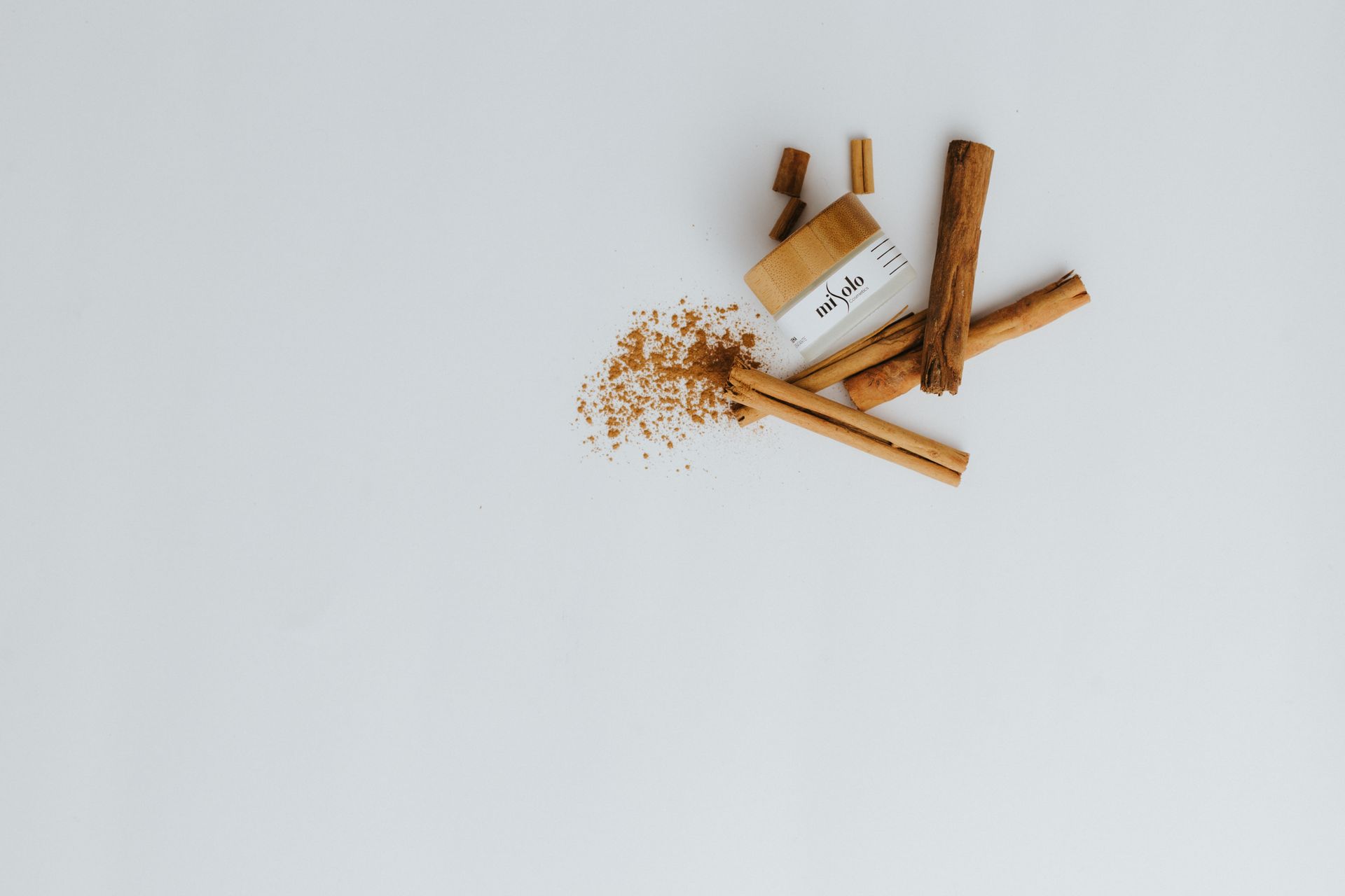 Minimalist flat lay of cinnamon sticks and powder on white background, perfect for food and spice themes.