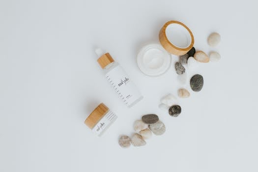 A flat lay of skincare bottles and jars with stones on a white background.