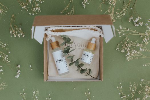 A beautifully arranged skincare set in eco-friendly packaging with dried flowers and eucalyptus on a green background.