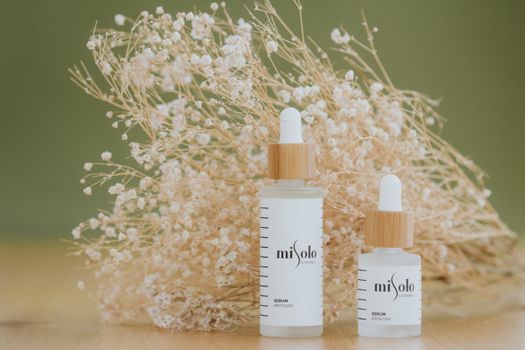 Elegant white skincare bottles on a table with delicate dried flowers, exuding natural beauty and purity.