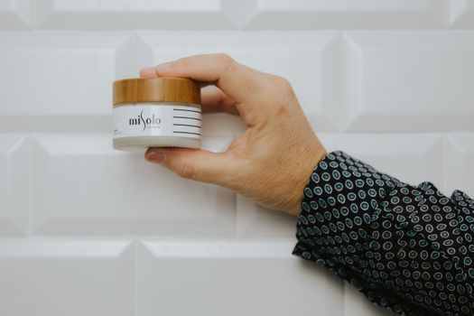Close-up of a hand holding a Misolo beauty product against a white tiled wall.