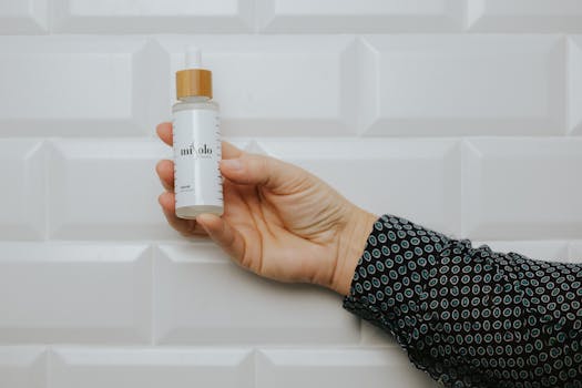 Close-up of an elegant hand holding a skincare serum bottle against a geometric background.