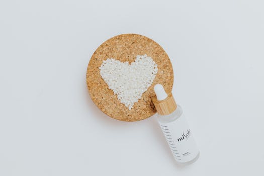 A minimalist flat lay featuring a serum bottle and a heart shape formed with small white beads on cork.