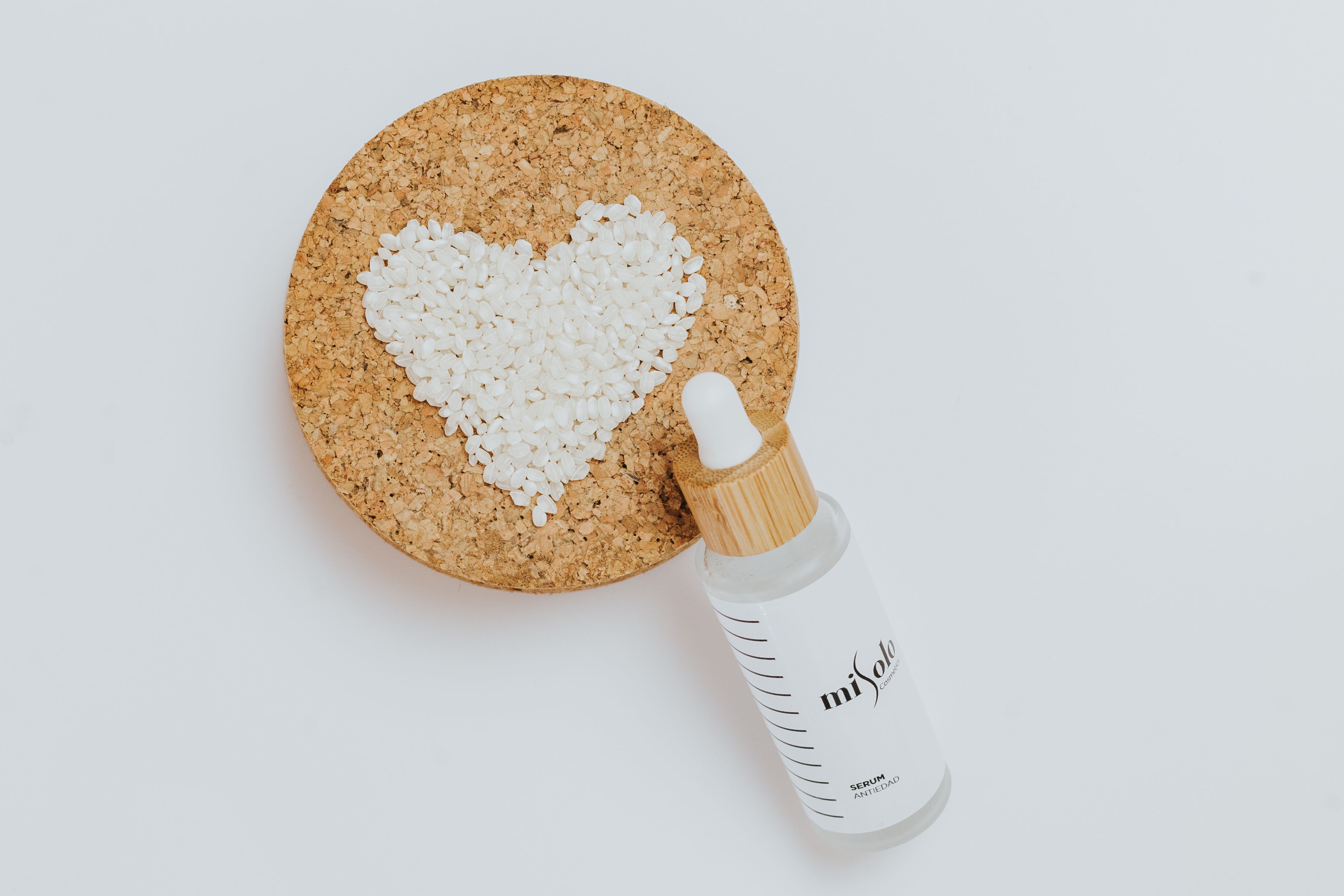 Flat lay of a cosmetic serum bottle with a heart shape on a cork board, evoking natural beauty.