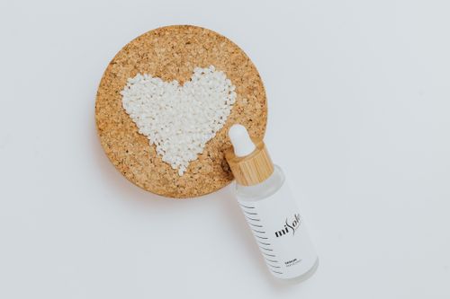 Free Flat lay of a cosmetic serum bottle with a heart shape on a cork board, evoking natural beauty. Stock Photo