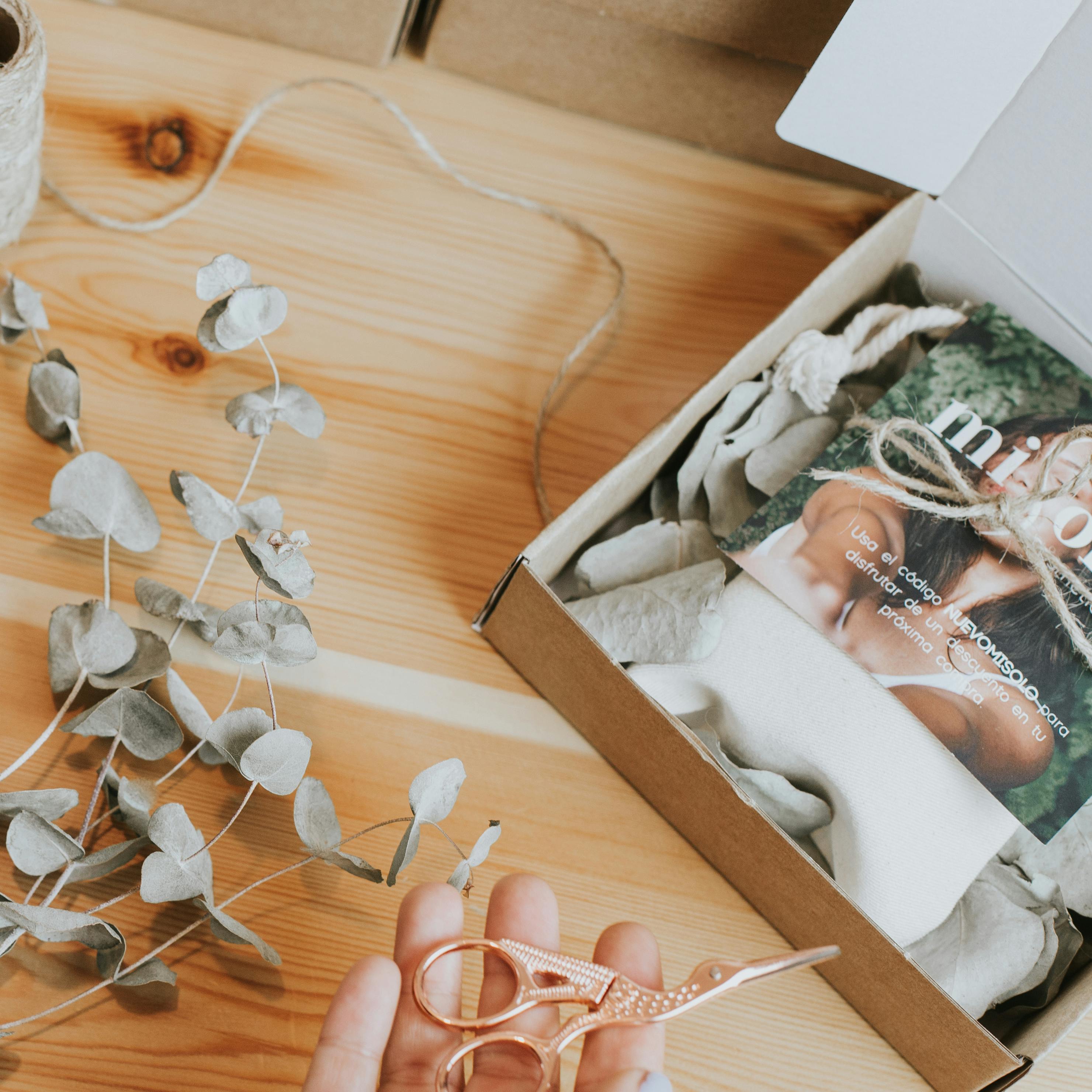 Top view of a handmade gift box with eucalyptus and ornate scissors on a wooden table.