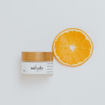 Luxurious skincare cream beside an orange slice on white background, perfect for beauty and wellness.