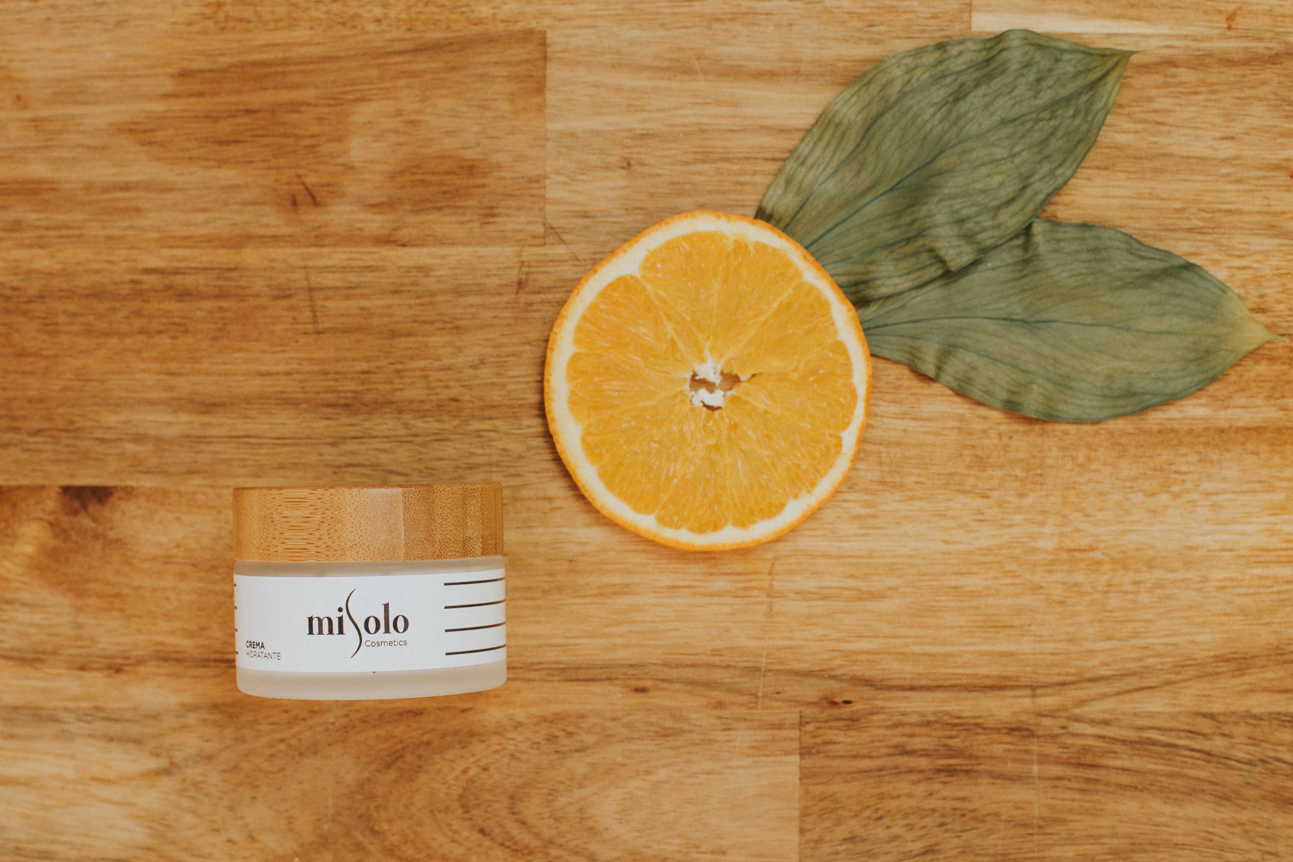 A cream jar with a slice of orange and leaves on a wooden surface, perfect for natural skincare concepts.