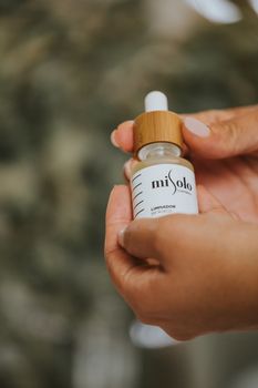 Hands holding a skincare serum bottle against a blurred background, highlighting natural beauty.