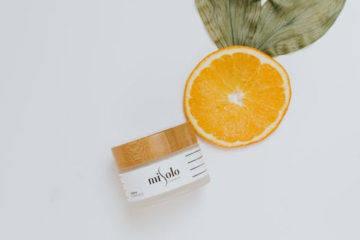 Close-up of orange slice and skincare jar with leaf on white background.