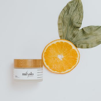 Overhead view of skincare cream with natural ingredients like orange and leaves for luxurious beauty.
