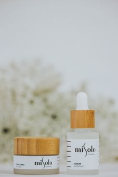 Close-up of Misolo cosmetics serum and cream with wooden accents on neutral background.