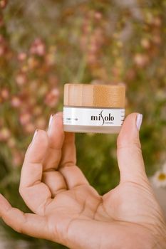 Close-up of a hand holding a Misolo cosmetic cream jar with a floral background.