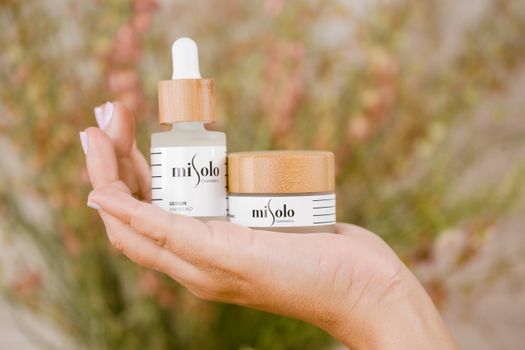 Close-up of hand holding natural skincare products, featuring serum and cream in eco-friendly packaging.