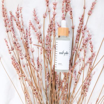 Minimalist product photo showing skincare serum bottle amidst dried pink flowers on a white surface.
