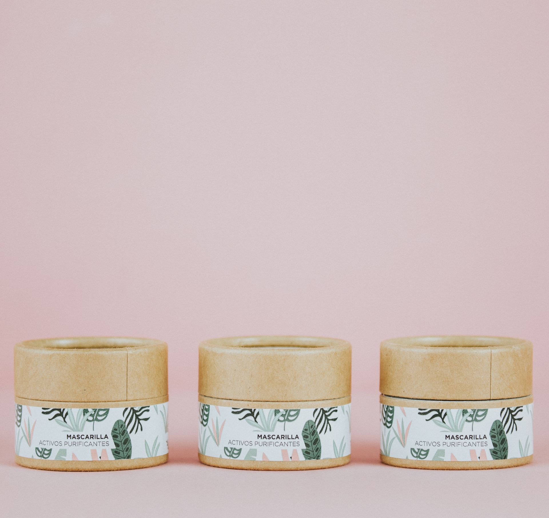 Three eco-friendly cosmetic jars with botanical labels against a pink backdrop.