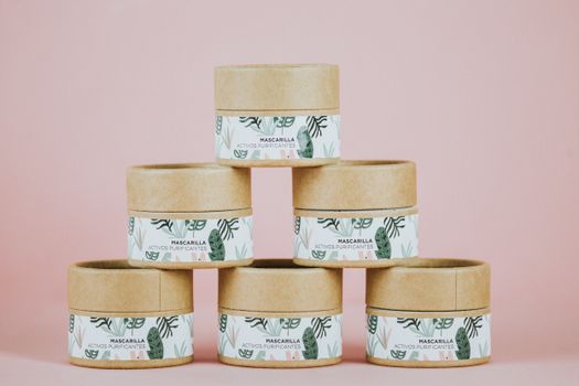 Stack of eco-friendly skincare jars on a pink backdrop, showcasing minimalist design.