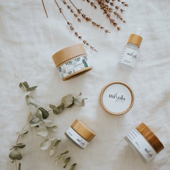 Minimalistic flatlay of eco-friendly beauty products with botanical elements on white fabric.