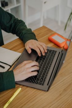 Hands typing on a laptop at a wooden desk with an external hard drive nearby.