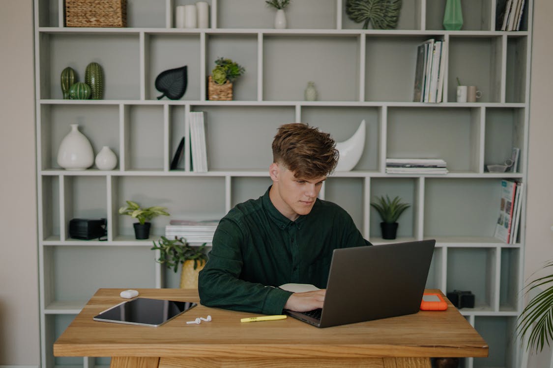 Free A Male Student in Green Long Sleeves Using a Laptop on a Wooden Desk Stock Photo