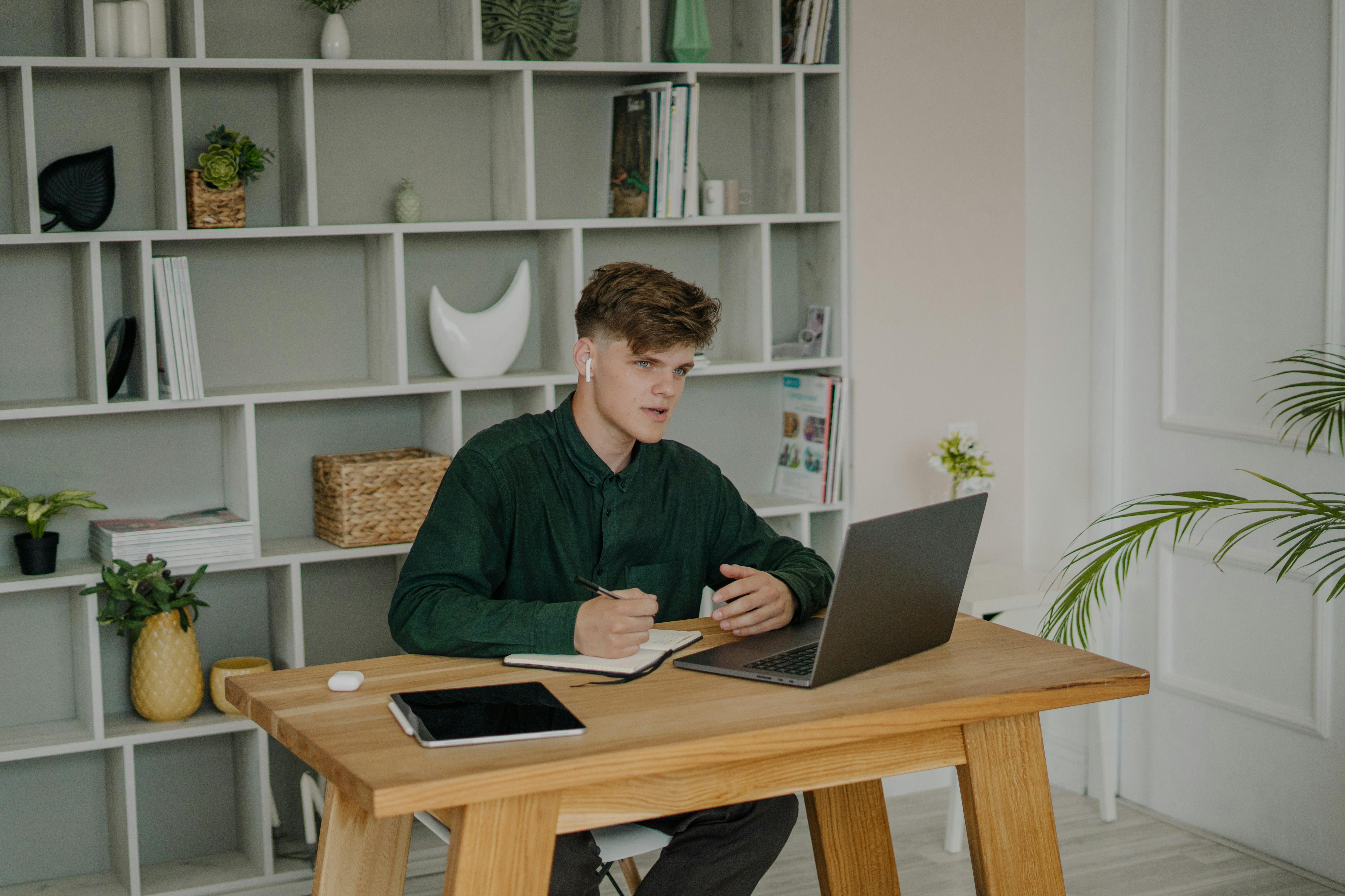 a male student in green long sleeves using a laptop on a wooden desk