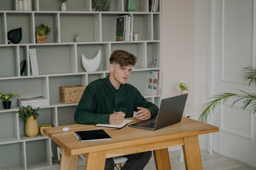 A Male Student in Green Long Sleeves Using a Laptop on a Wooden Desk