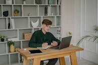 A Male Student in Green Long Sleeves Using a Laptop on a Wooden Desk