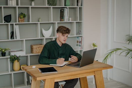 A young man engaged in online learning at home using a laptop and headphones.