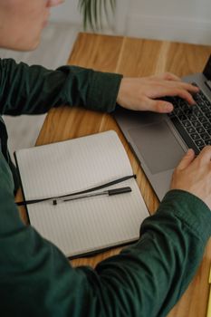 Adult working on a laptop with a notebook on a wooden desk, ideal for productivity themes.